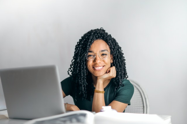 imagen de una chica morena con rulos, y con una laptop, sonriendo